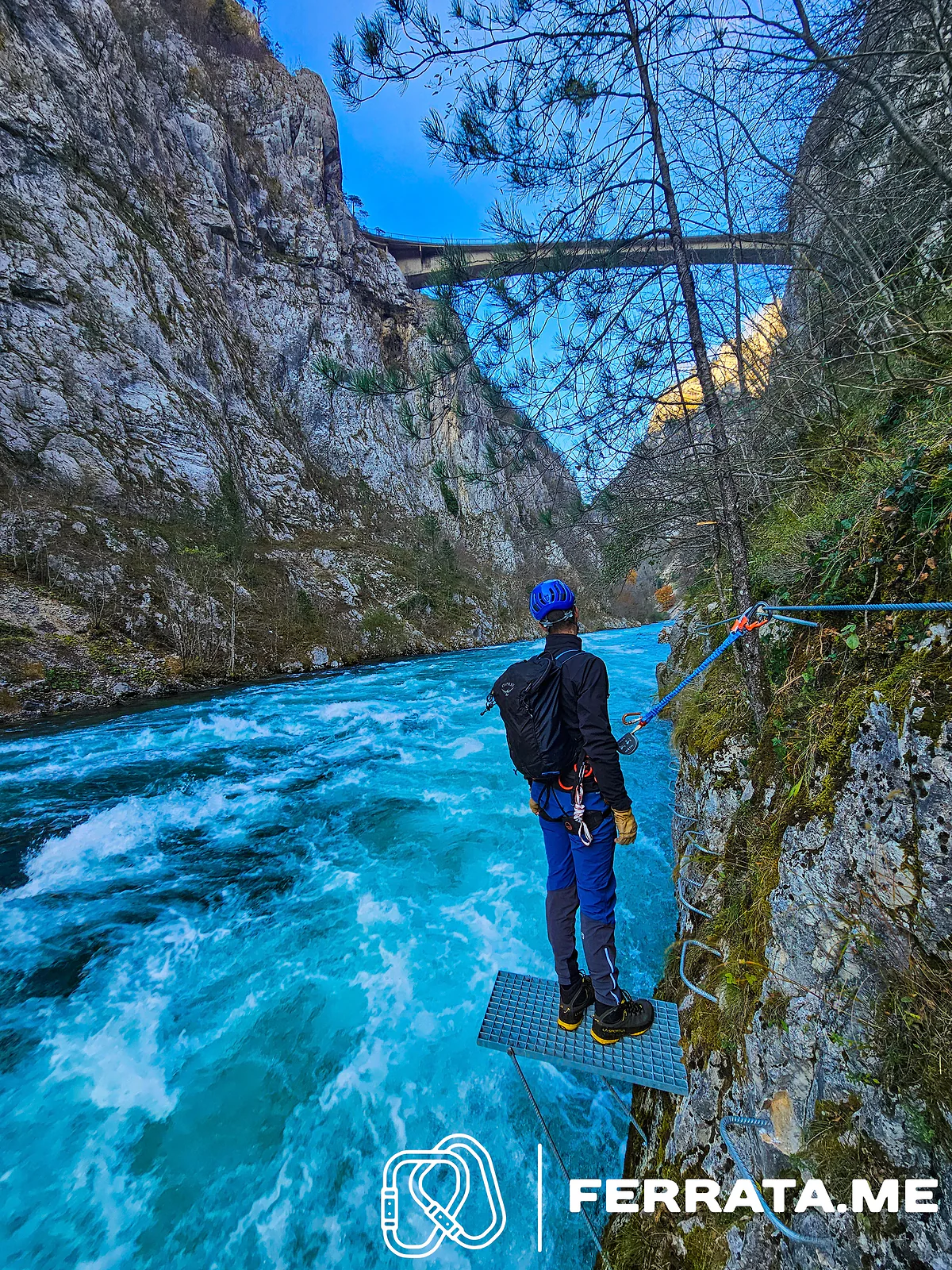 A man standing on a steel grate above white water, with the bridge high above.