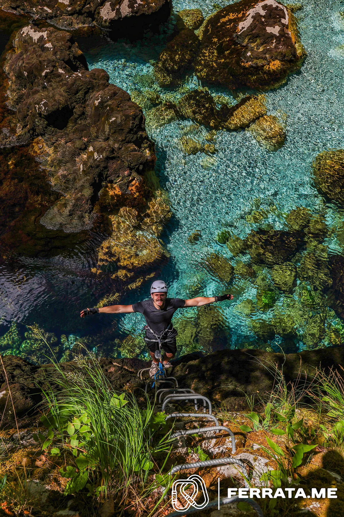 A climber seen from above with arms spread wide over clear water.