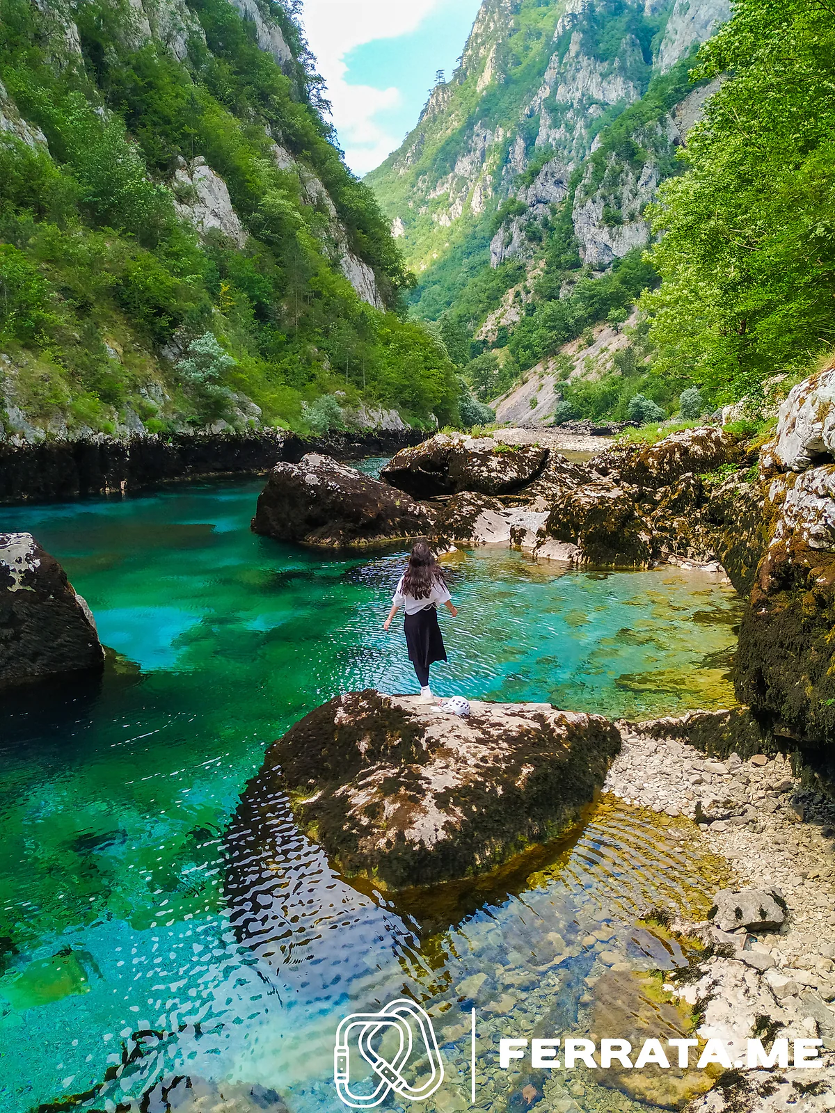 A person standing on a boulder in a turquoise pool in the canyon.